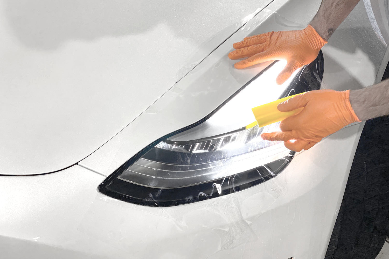 Person fixing the headlights of a white Tesla car