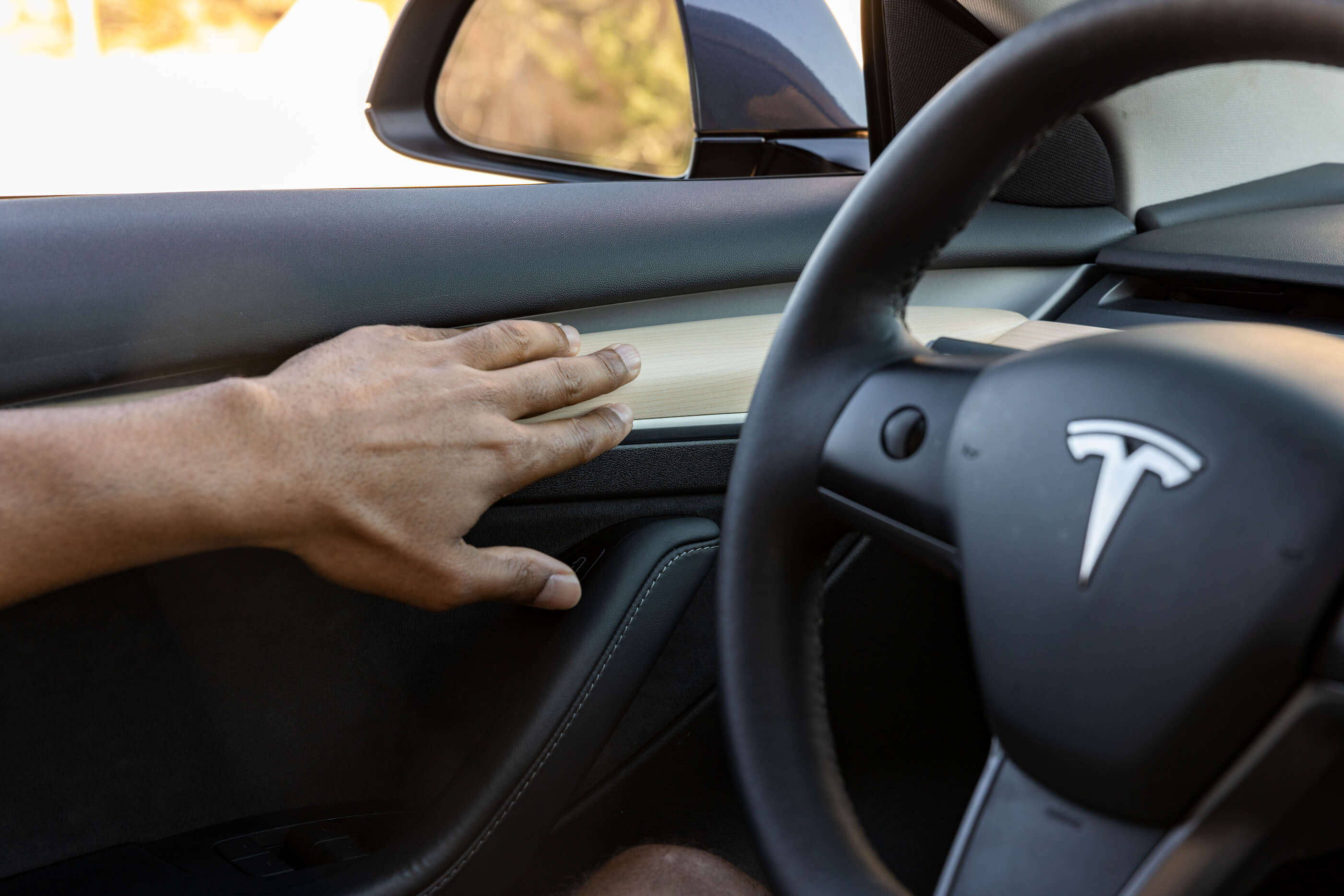 A hand gently touches the door of a Tesla car